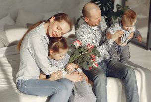 Cheerful parents with children wearing casual clothes smiling while playing with daughter and son in bedroom together during weekend at home